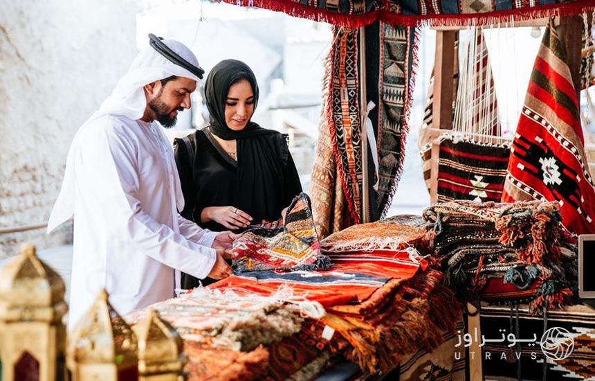یک زن و مرد جوان عرب درحال خرید از غرفه‌ی فروش فرش و گلیم سنتی